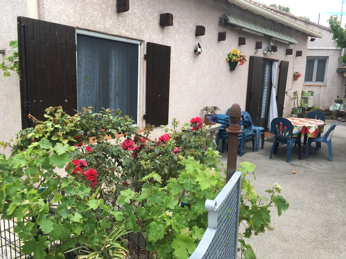 Maison de plain-pied de l'avenue de la Gare : rosiers en fleurs devant une fenêtre aux volets bruns, cour avec table et chaises de jardin
