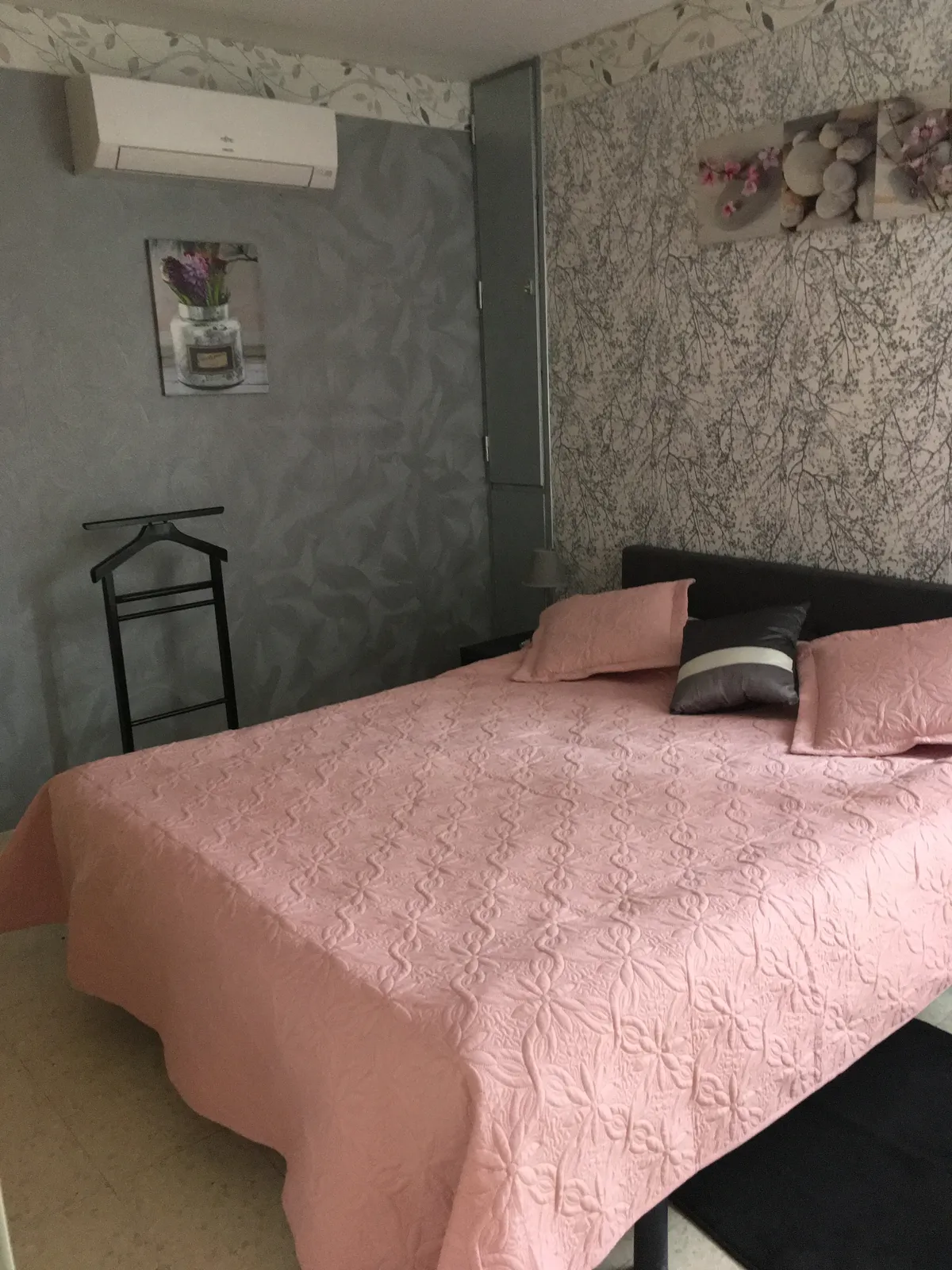 Chambre de l'appartement Thermes 2 : lit double au couvre-lit rose matelassé et climatisation